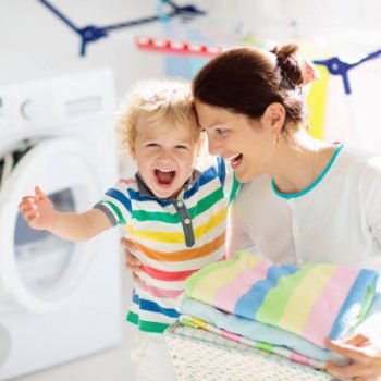 Mother and kids in laundry room with washing machine or tumble dryer. Family chores. Modern household devices and washing detergent in white sunny home. Clean washed clothes on drying rack.